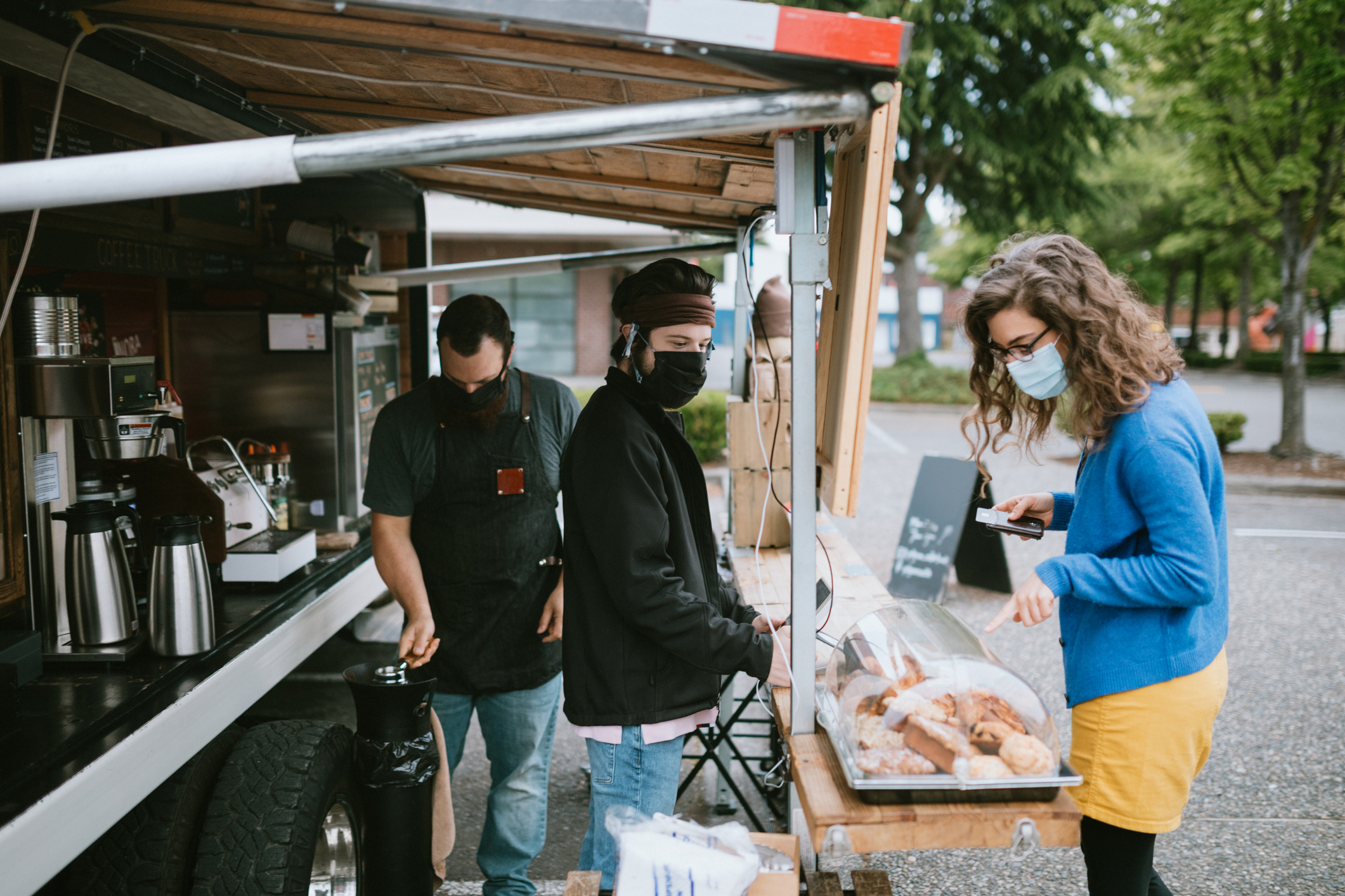 Masked Customer Orders Coffee And Snacks at Food Truck A young man takes the order of a woman at a coffee food cart in the Seattle, Washington area. The outdoor setting is ideal for people to still purchase their coffee and espresso drinks while maintaining social distance during the Coronavirus pandemic.
